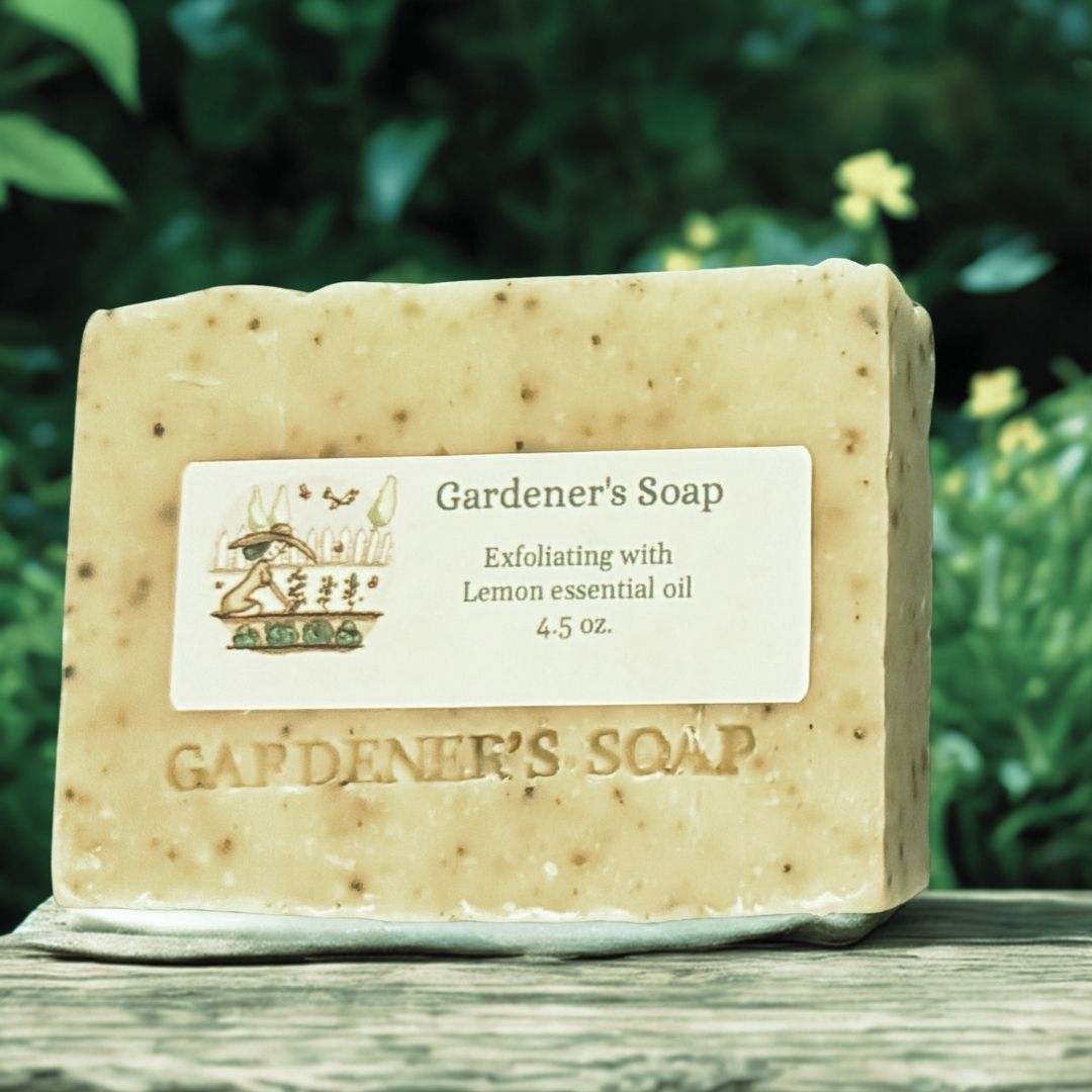 A rectangular bar of exfoliating lemon scented Gardener's Soap  resting on a weathered wooden surface with a blurred green garden background.