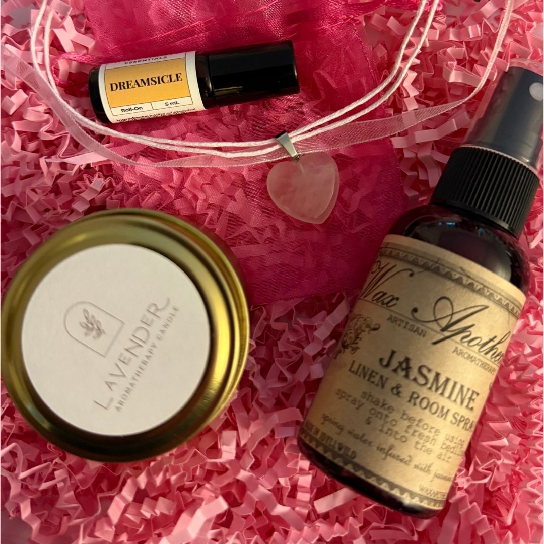 Collection of beauty products including a candle, essential oil bottle, and linen spray on pink crinkled paper.